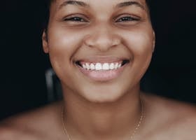 Bright portrait of a smiling woman, exuding warmth and positivity, set against a dark background.